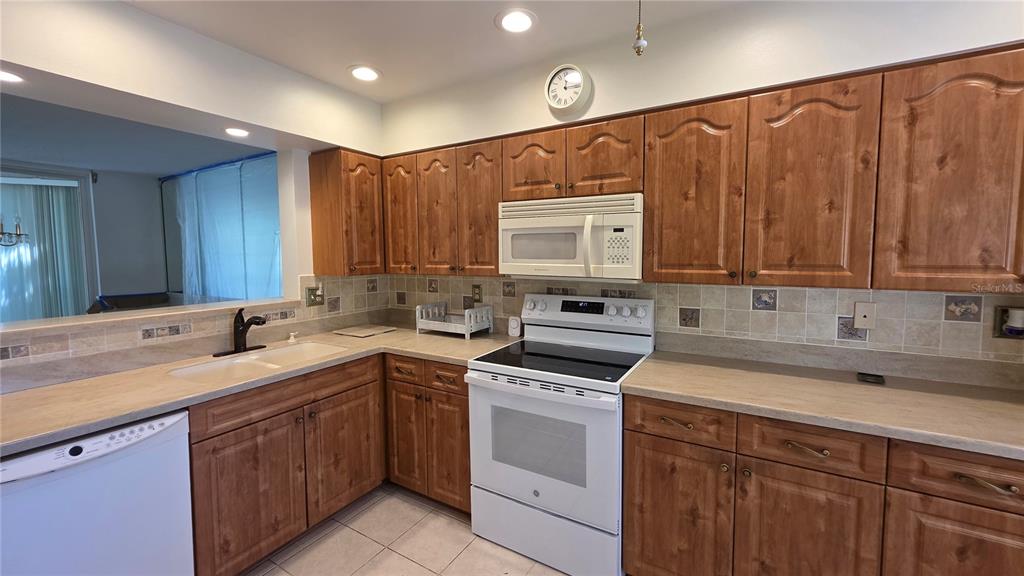 A kitchen features wood cabinets, white appliances, and a beige countertop with a tiled backsplash — 6101 34TH ST W UNIT 27C, BRADENTON, FL