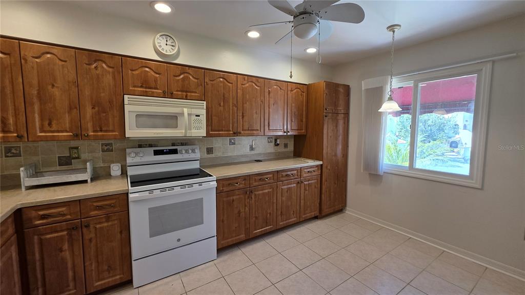 A kitchen features wood cabinets, white appliances, tile flooring, and a window with a view — 6101 34TH ST W UNIT 27C, BRADENTON, FL