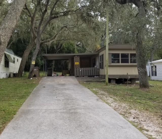 A tan mobile home with a carport and a concrete driveway sits among large trees — 1715 INDIAN TRAIL, LEESBURG, FL