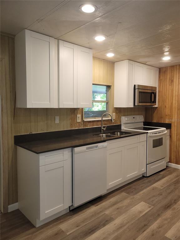 A kitchen features white cabinets, dark countertops, a dishwasher, and wood-paneled walls — 1715 INDIAN TRAIL, LEESBURG, FL
