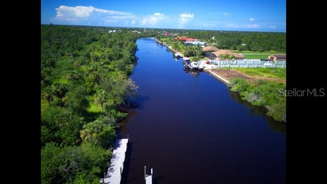 An aerial view shows a canal bordered by dense trees on one side and houses — 1140 HOFFER STREET, PORT CHARLOTTE, FL