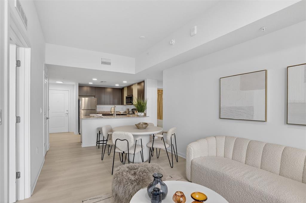 A modern open-concept living and dining area features a white sofa, round table, and kitchen — 5579 MILLENIA PARK BOULEVARD UNIT 421, ORLANDO, FL