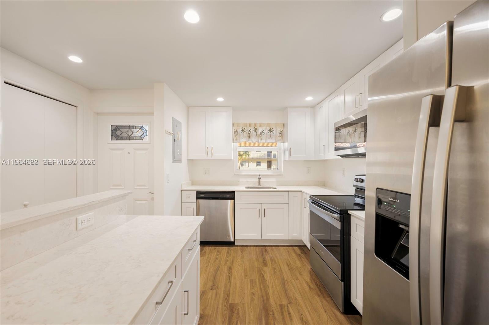 A modern kitchen features white cabinets, stainless steel appliances, and light wood-look flooring — 750 SE 6th Ave # 223, Deerfield Beach FL 33441, DEERFIELD BEACH, FL