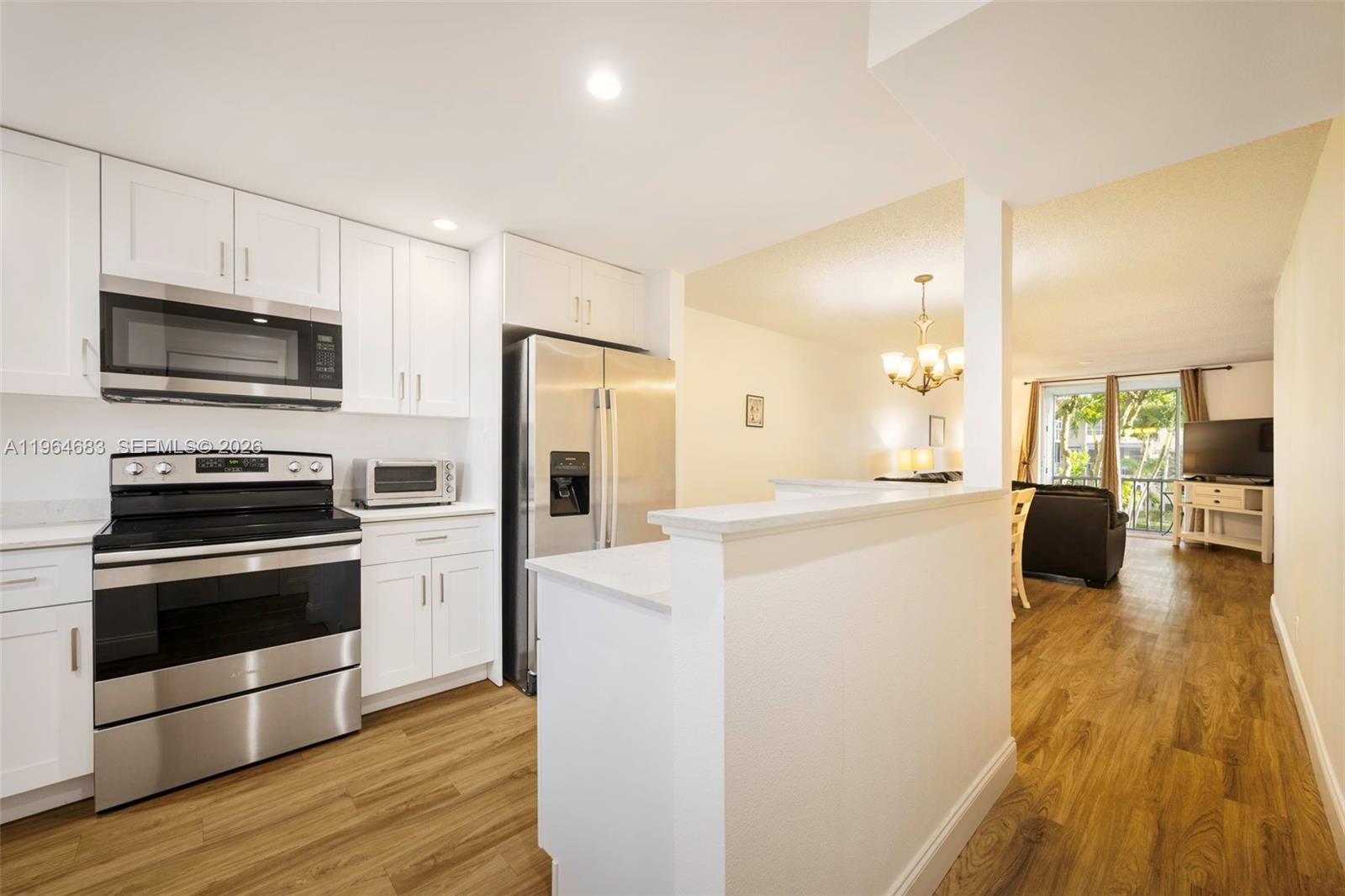 A kitchen with white cabinets and stainless steel appliances opens to a living area — 750 SE 6th Ave # 223, Deerfield Beach FL 33441, DEERFIELD BEACH, FL