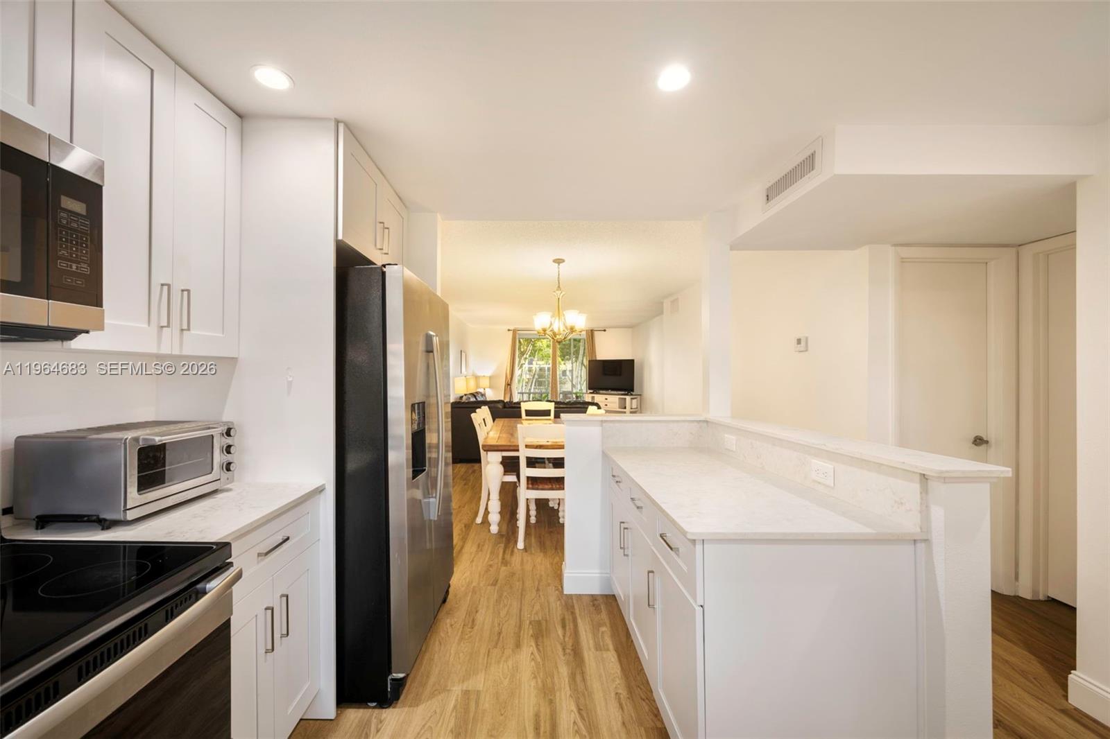 A white kitchen with stainless steel appliances opens into a dining area and living room — 750 SE 6th Ave # 223, Deerfield Beach FL 33441, DEERFIELD BEACH, FL