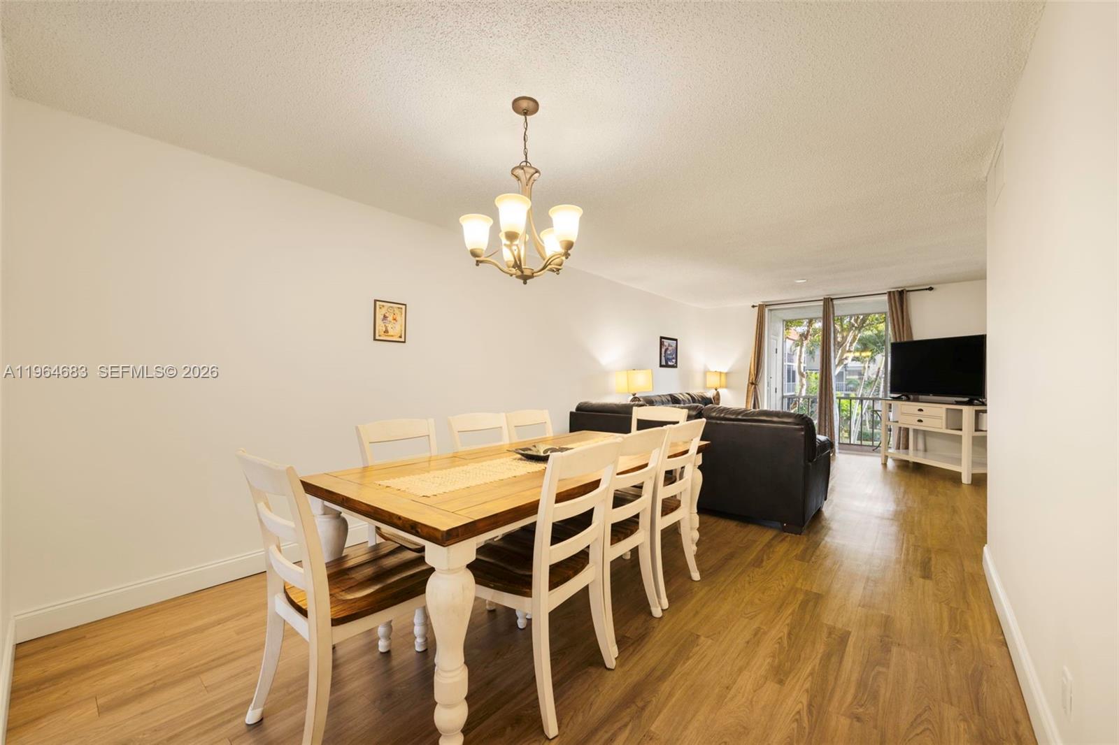 A dining area with a wooden table and white chairs sits before a living room — 750 SE 6th Ave # 223, Deerfield Beach FL 33441, DEERFIELD BEACH, FL