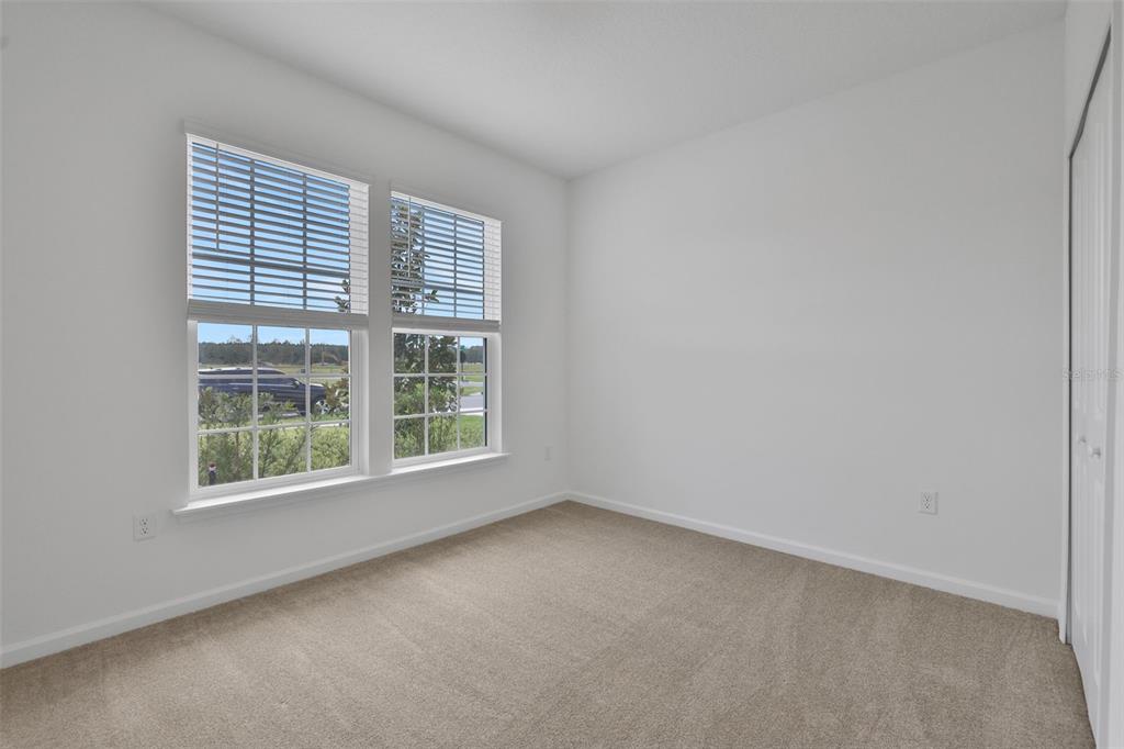 An empty bedroom features white walls, beige carpeting, and two windows overlooking a street — 3932 HOLSTEIN WAY, GREEN COVE SPRINGS, FL