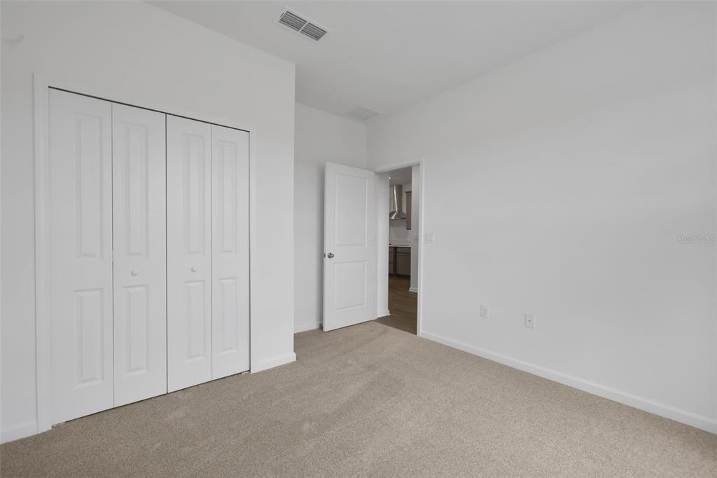 A bedroom with beige carpet, white walls, a bi-fold closet, and an open doorway — 3932 HOLSTEIN WAY, GREEN COVE SPRINGS, FL