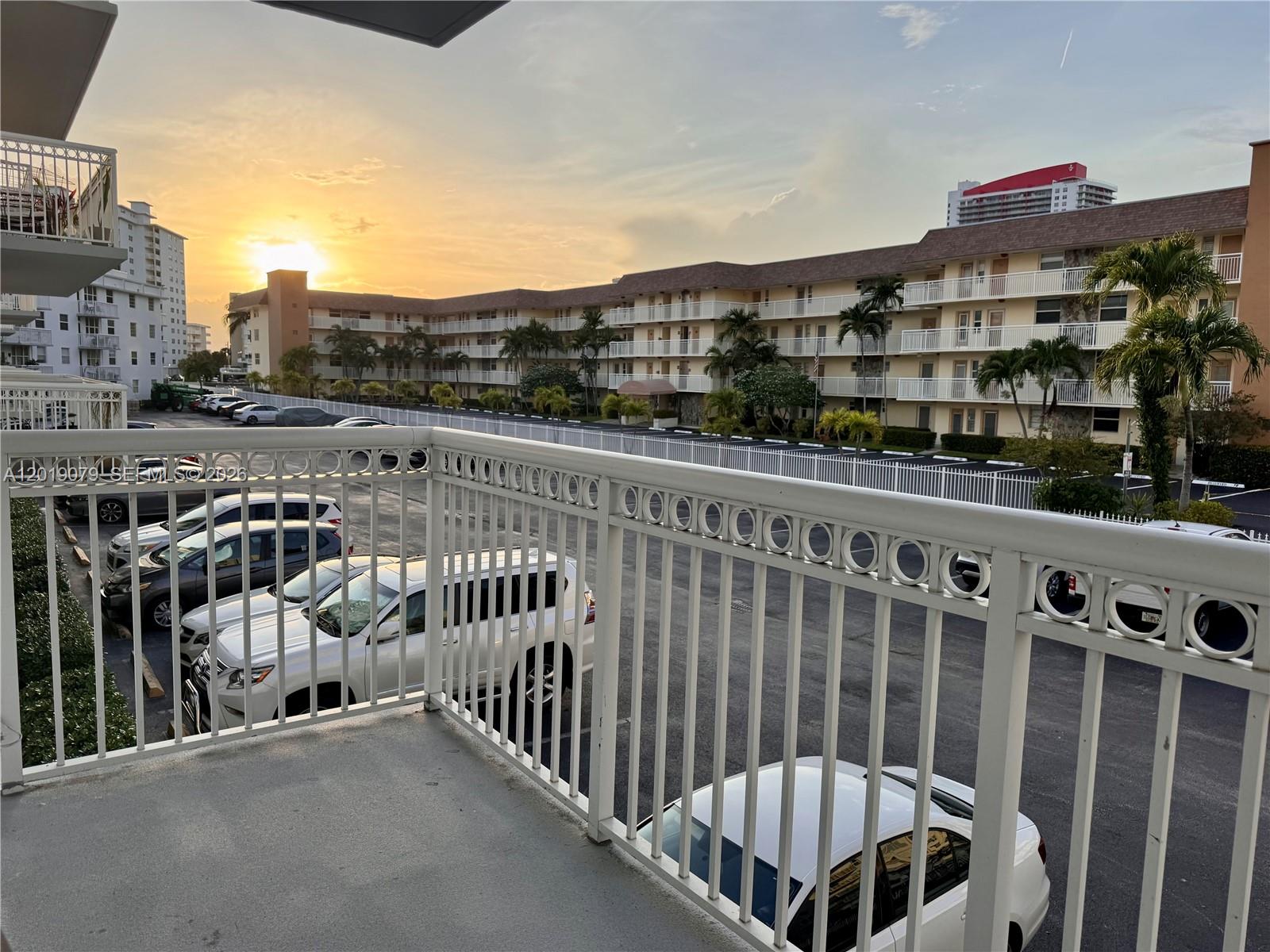 A balcony view overlooks a parking lot and apartment buildings during a sunset — 1913 S Ocean Dr # 212, Hallandale Beach FL 33009, HALLANDALE BEACH, FL