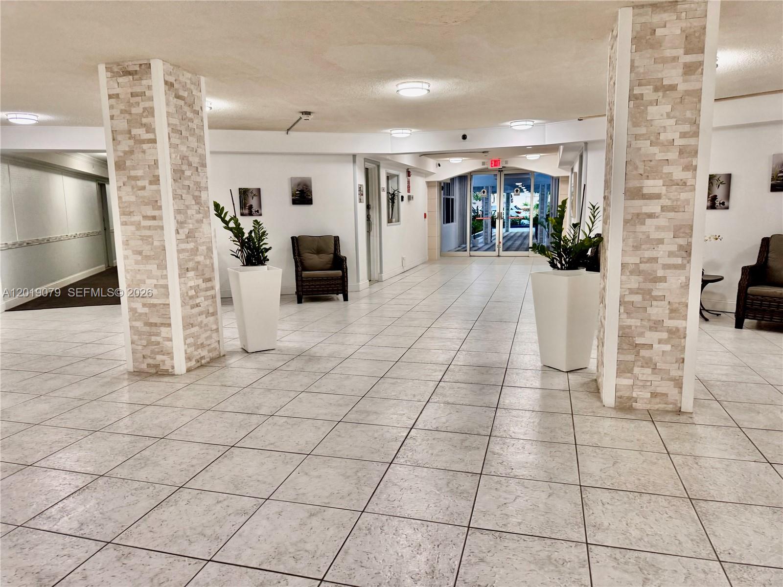 A tiled lobby features two stone-clad columns, potted plants, and glass doors leading outside — 1913 S Ocean Dr # 212, Hallandale Beach FL 33009, HALLANDALE BEACH, FL
