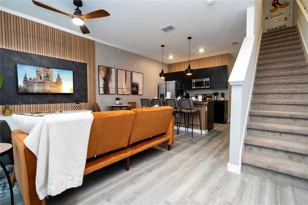 A modern open-concept living room and kitchen featuring wood-slat walls and a staircase — 3369 TRANQUIL TRAIL, KISSIMMEE, FL
