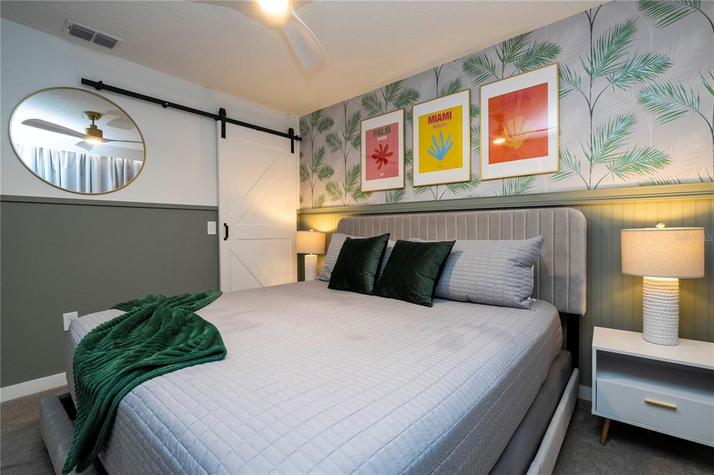 A bedroom features a gray bed, palm-print wallpaper, a barn door, and three framed prints — 3369 TRANQUIL TRAIL, KISSIMMEE, FL