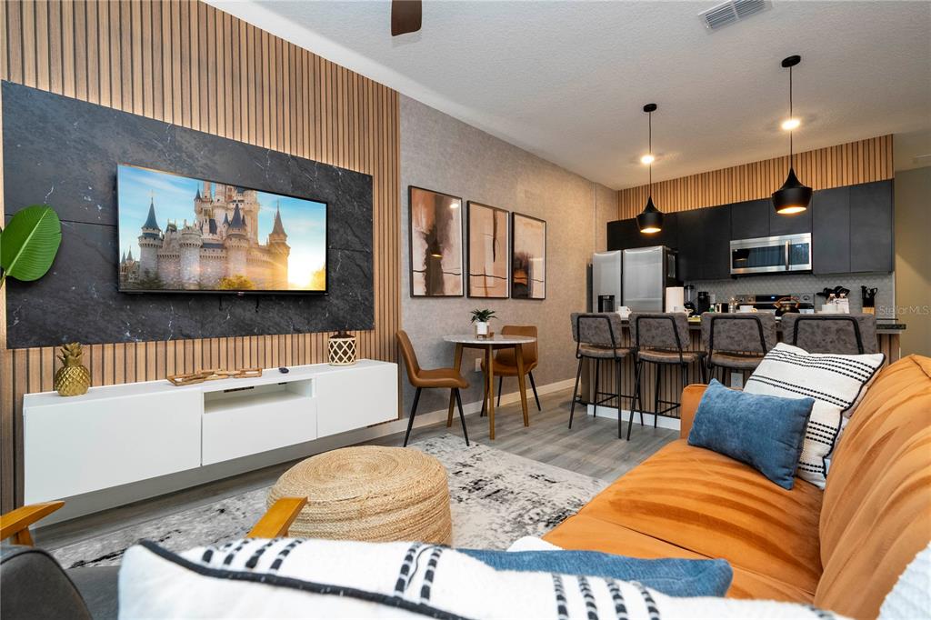 A modern living room and kitchen area with wood slat walls, dark cabinetry, and furniture — 3369 TRANQUIL TRAIL, KISSIMMEE, FL