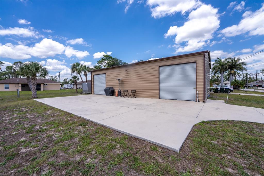 A tan metal garage with two roll-up doors sits on a large concrete driveway — 2089 MAUVE TERRACE, NORTH PORT, FL