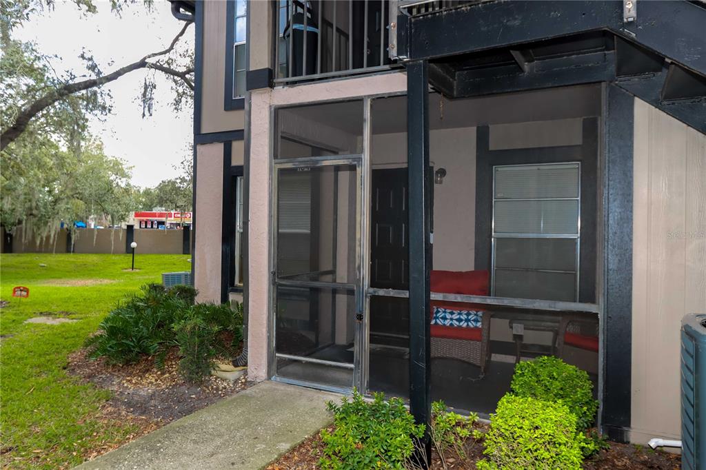 A ground-level apartment patio features a screen enclosure, a black door, and outdoor furniture — 4009 NESTLE OAKS PLACE UNIT 104, TAMPA, FL