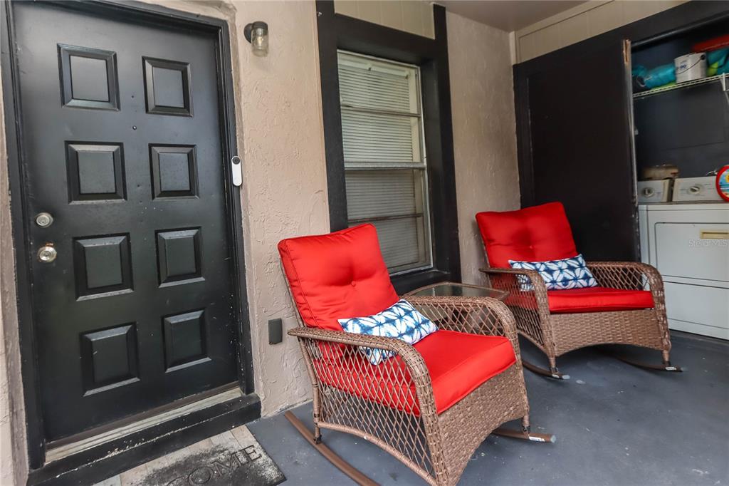 A covered patio features two wicker rocking chairs with red cushions and a laundry closet — 4009 NESTLE OAKS PLACE UNIT 104, TAMPA, FL