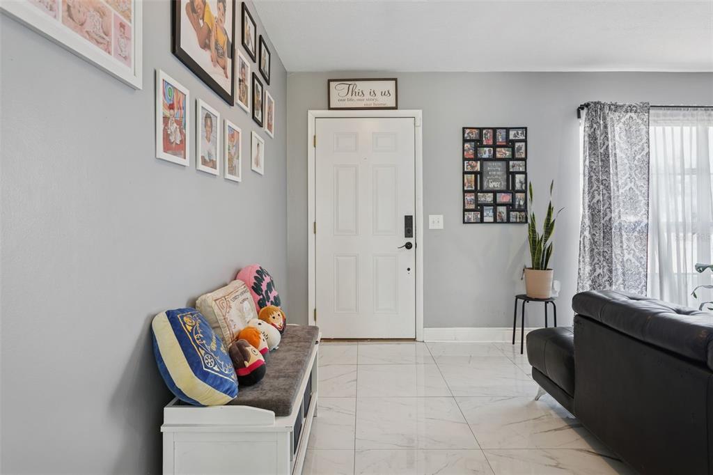 A bright entryway features light gray walls, white tile flooring, a storage bench, and wall decor — 1614 BERKSHIRE DRIVE, BRANDON, FL