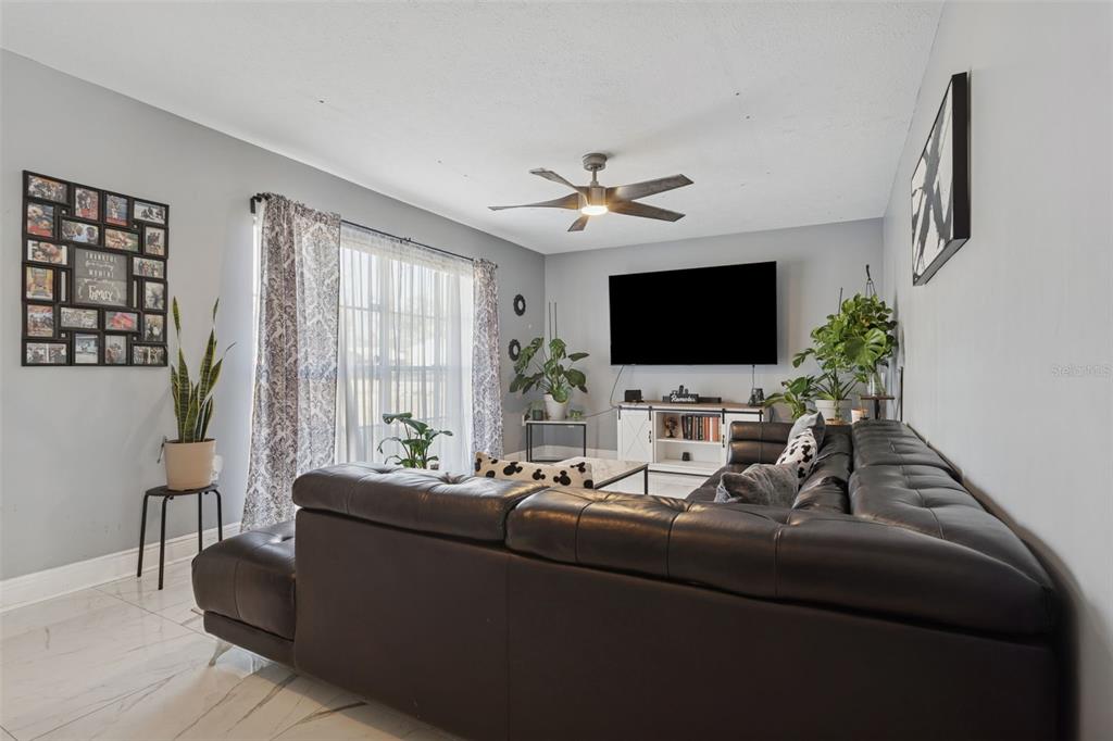 A living room features a large black sectional sofa, a wall-mounted television, and tile flooring — 1614 BERKSHIRE DRIVE, BRANDON, FL