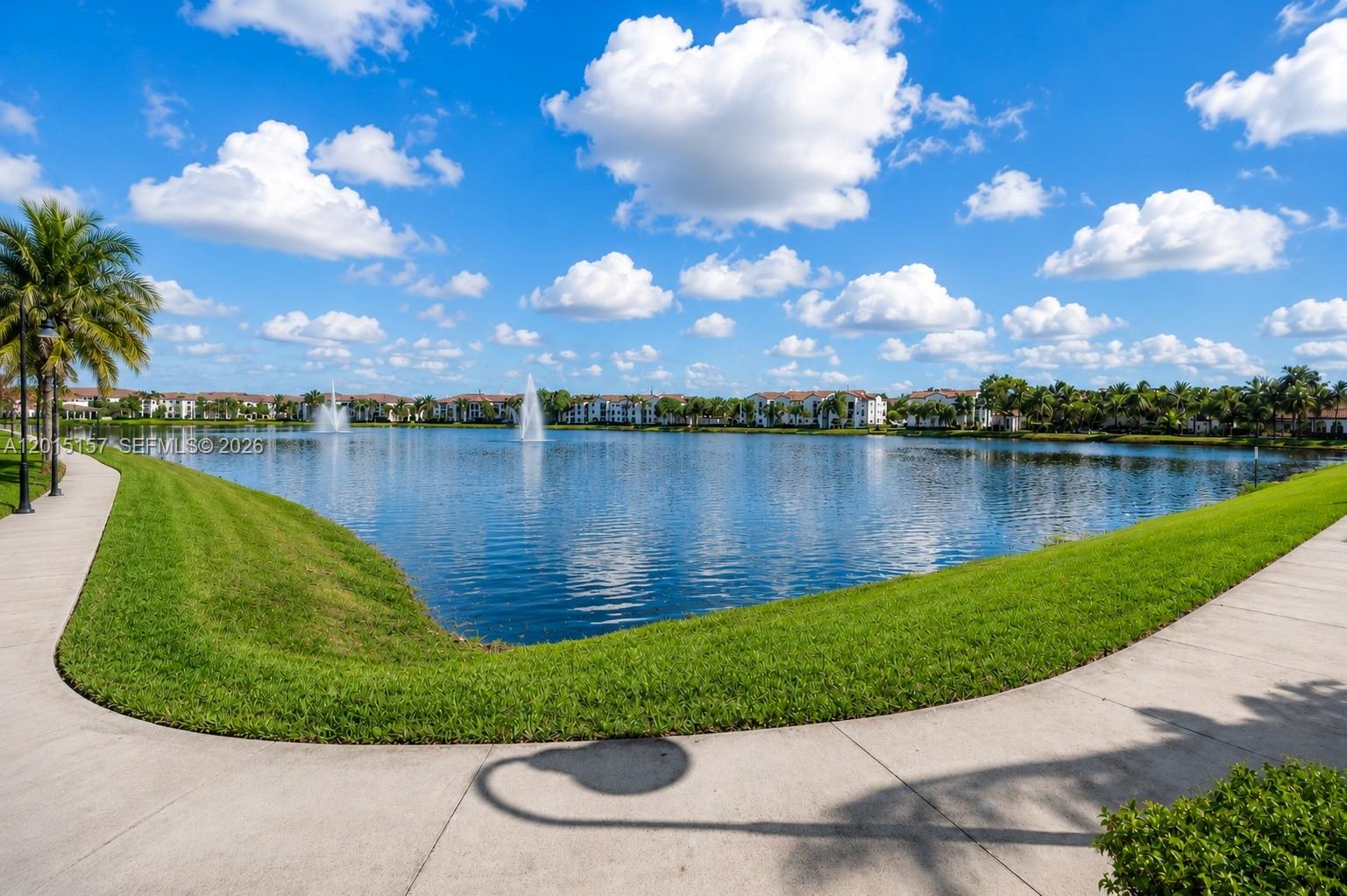 A paved walkway curves around a large lake with fountains and apartment buildings in the background — 2709 SW 119th Way # 2709, Miramar FL 33025, MIRAMAR, FL