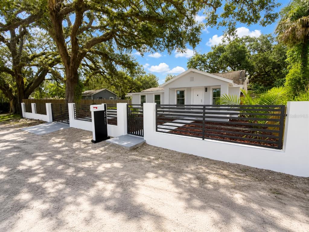 A single-story house with a white stucco exterior is enclosed by a modern horizontal fence — 4311 N 25TH STREET, TAMPA, FL