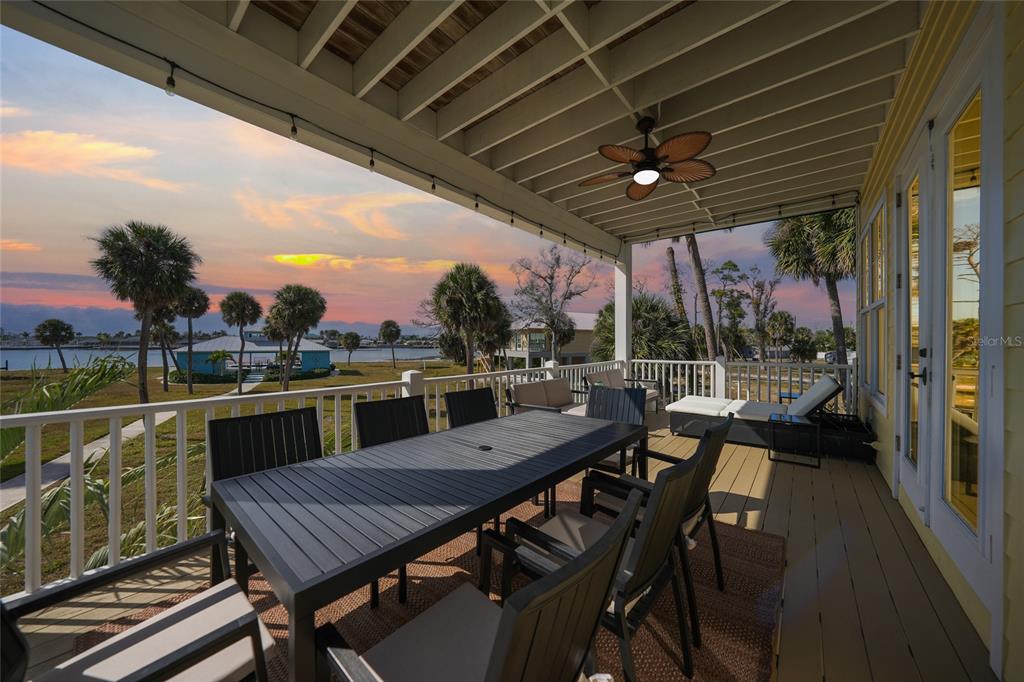 A covered outdoor deck features a dining table, lounge chairs, and a scenic waterfront view — 6751 PORTSIDE LANE, ENGLEWOOD, FL