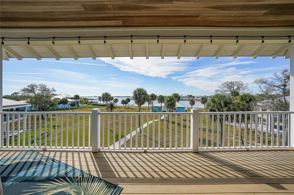 A covered wooden deck with a white railing overlooks a grassy yard and the water — 6751 PORTSIDE LANE, ENGLEWOOD, FL