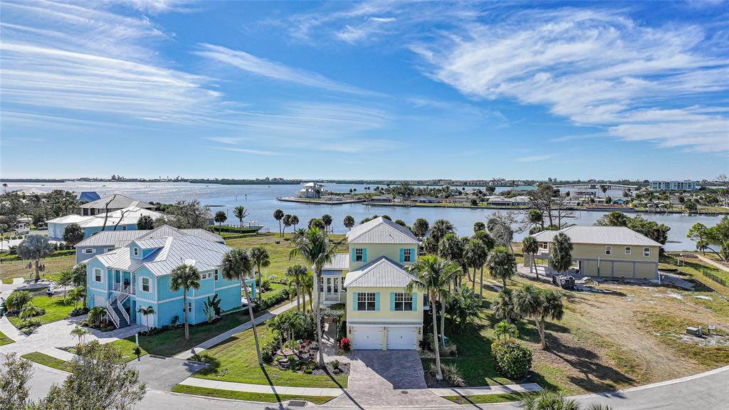 An aerial view shows three coastal-style houses with metal roofs near a body of water — 6751 PORTSIDE LANE, ENGLEWOOD, FL