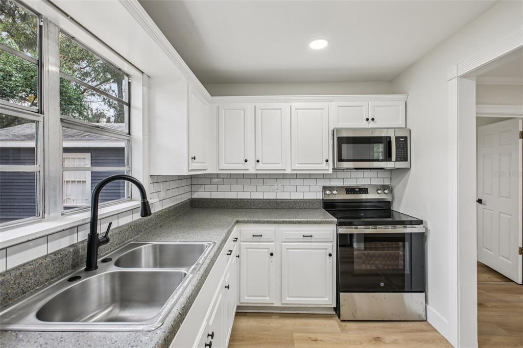 A kitchen with white cabinets, gray countertops, a stainless steel stove, and a double sink — 5808 N 17TH STREET, TAMPA, FL