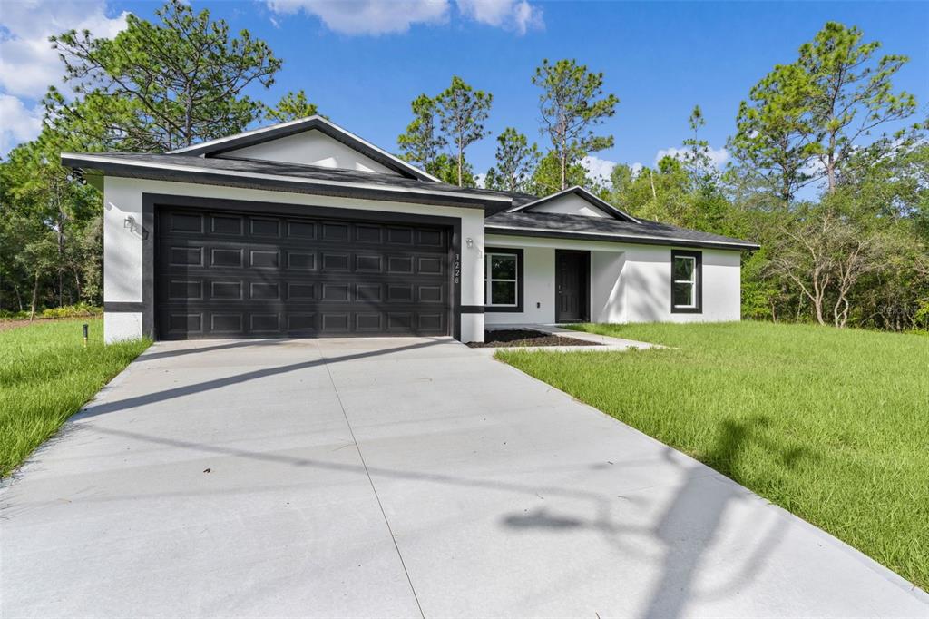 A single-story house with white stucco walls, a dark garage door, and a concrete driveway — 3228 W CAMILO DRIVE, CITRUS SPRINGS, FL