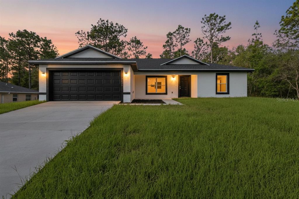 A single-story house with a white exterior, black trim, and a two-car garage at dusk — 3228 W CAMILO DRIVE, CITRUS SPRINGS, FL