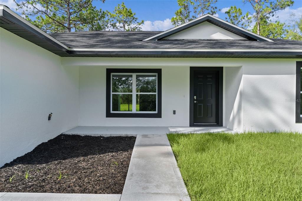 A white house exterior features a black front door, dark window trim, and a walkway — 3228 W CAMILO DRIVE, CITRUS SPRINGS, FL