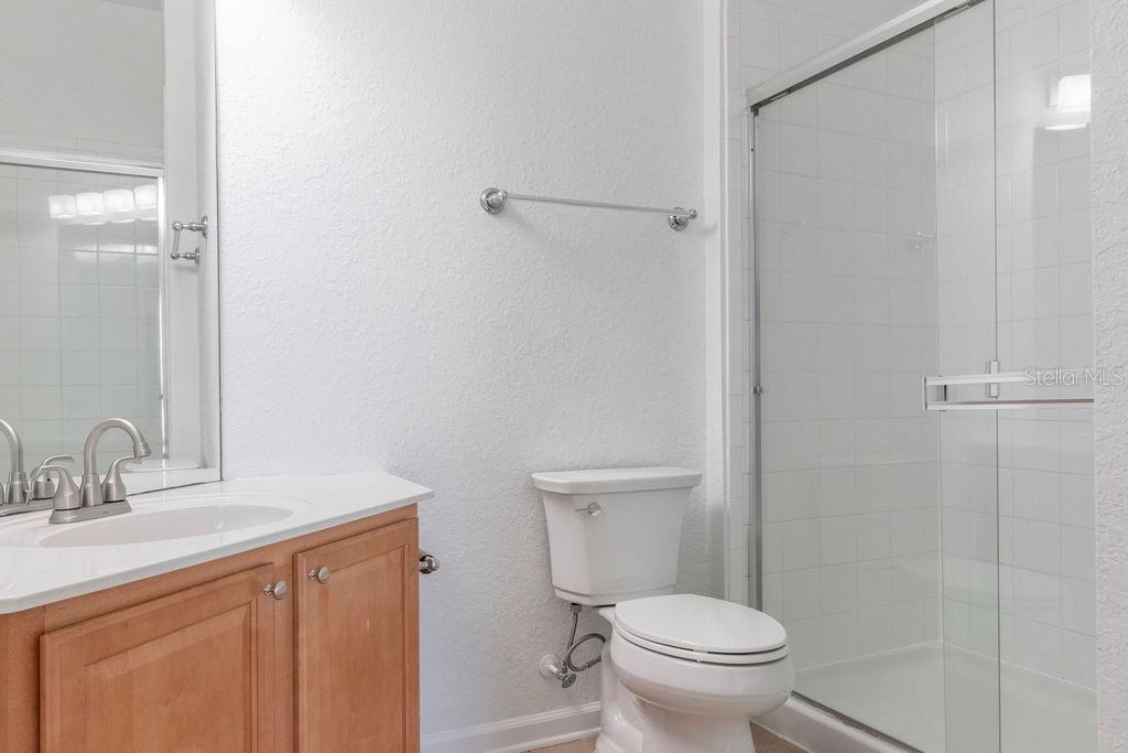A bathroom features a wooden vanity, a white toilet, and a glass-enclosed shower — 3868 LEXMARK LANE UNIT 409, ROCKLEDGE, FL