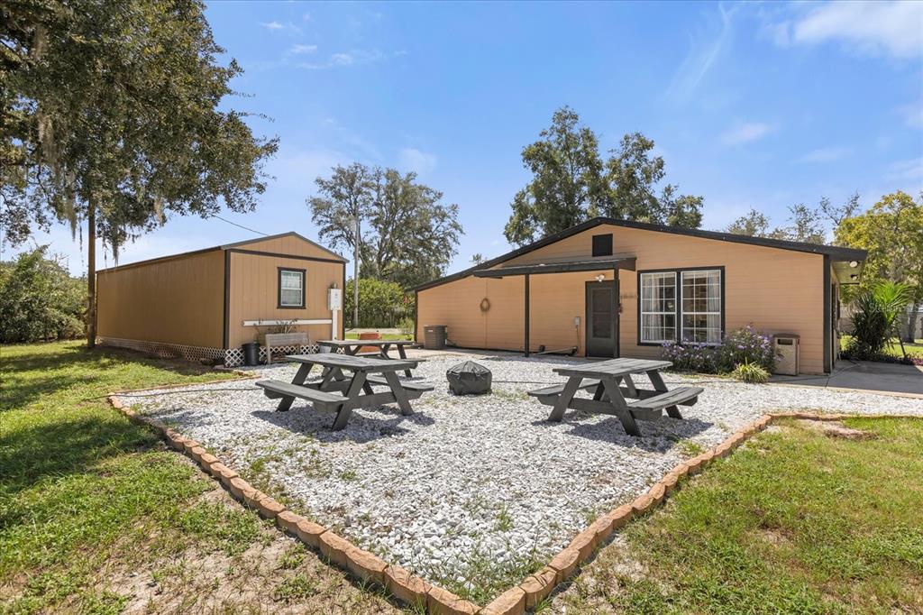 A tan house with a detached shed and two picnic tables on a gravel patio — 14043 TENNESSEE AVENUE, ASTATULA, FL