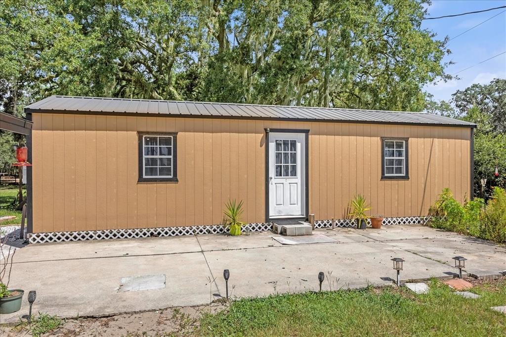 A tan, single-story rectangular structure with a metal roof sits on a concrete patio — 14043 TENNESSEE AVENUE, ASTATULA, FL