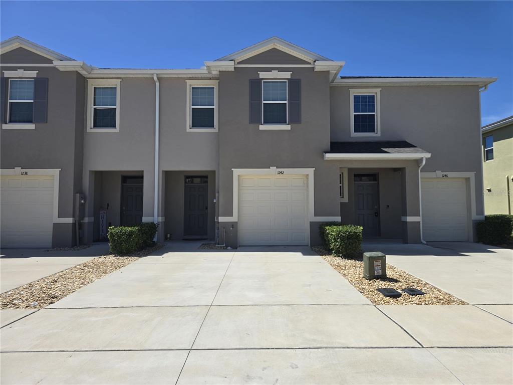 A row of three attached townhomes features gray stucco siding, white garage doors, and concrete driveways — 1242 LIDO DRIVE, HOWEY IN THE HILLS, FL
