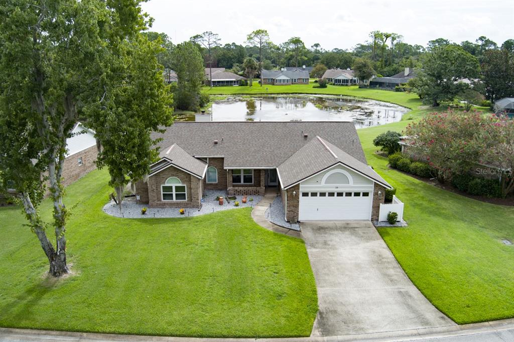 An aerial view shows a single-story brick house with a two-car garage and a pond — 18 CARRIAGE CREEK WAY, ORMOND BEACH, FL