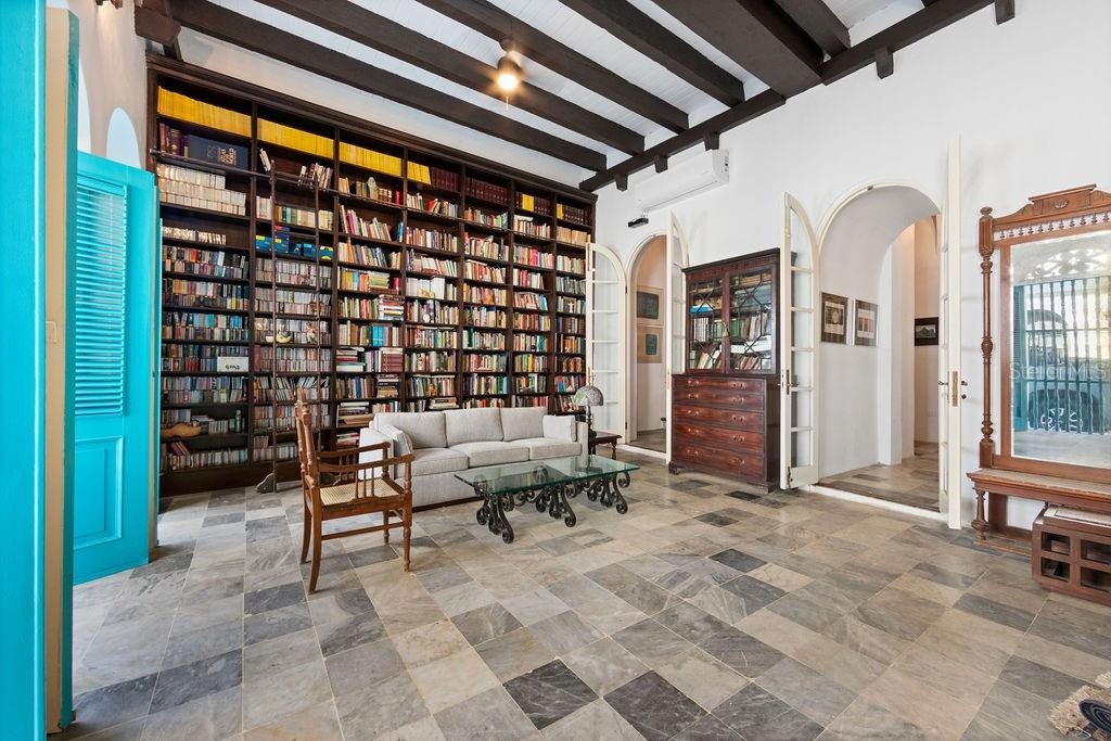 A library room features floor-to-ceiling bookshelves, exposed dark wood ceiling beams, and stone tile flooring — 50 SAN FRANCISCO ST, SAN JUAN, PR