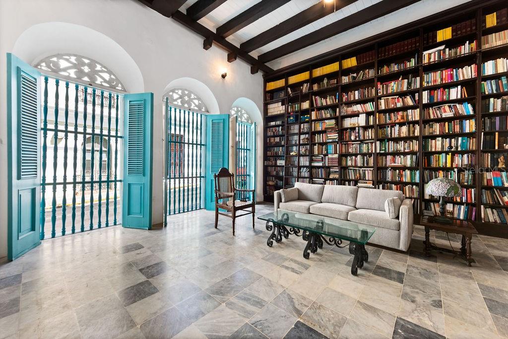 A library with a sofa, glass coffee table, floor-to-ceiling bookshelves, and blue shuttered doors — 50 SAN FRANCISCO ST, SAN JUAN, PR