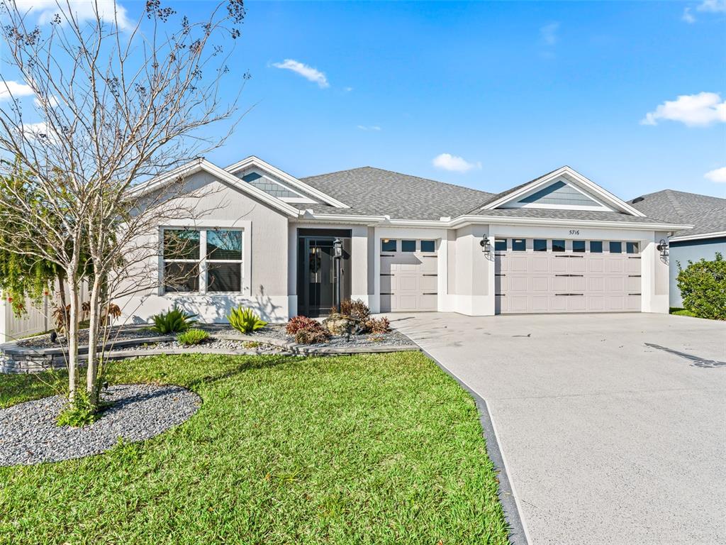 A single-story house with a gray exterior, a three-car garage, and a landscaped front yard — 5716 MELVIN DRIVE, THE VILLAGES, FL