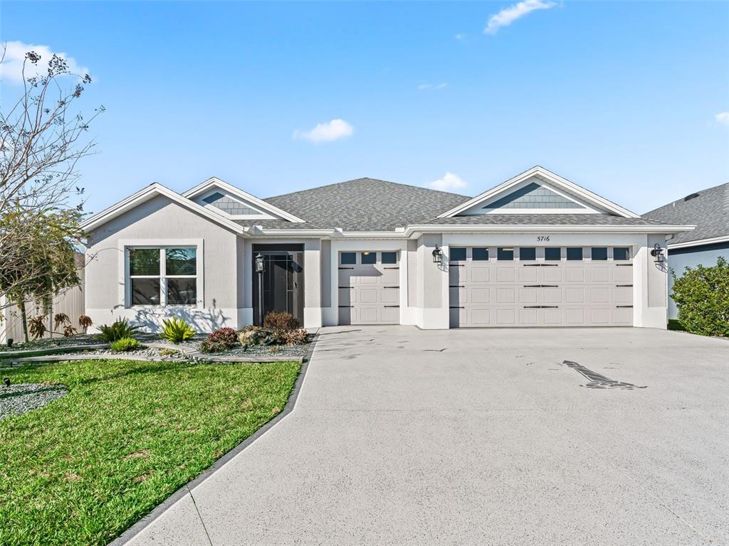 A single-story house with a gray stucco exterior, a three-car garage, and a concrete driveway — 5716 MELVIN DRIVE, THE VILLAGES, FL