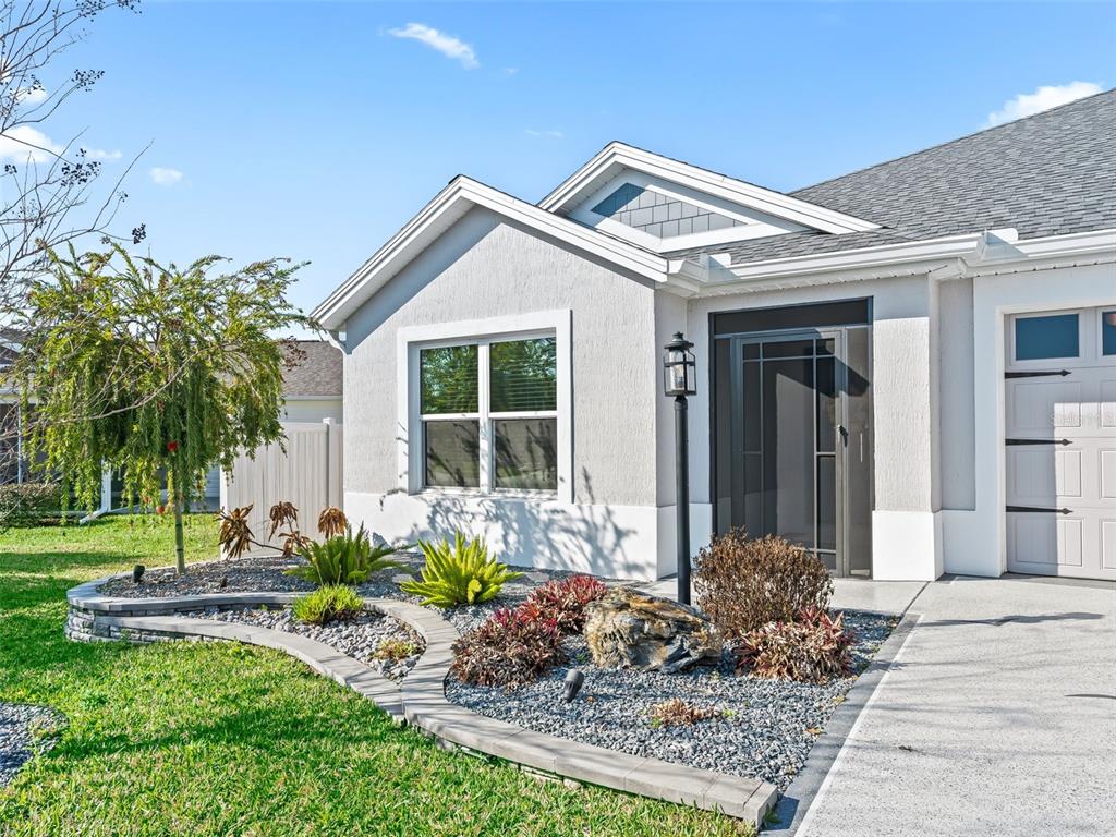 A light-colored house exterior features a landscaped front garden with a stone-bordered bed — 5716 MELVIN DRIVE, THE VILLAGES, FL