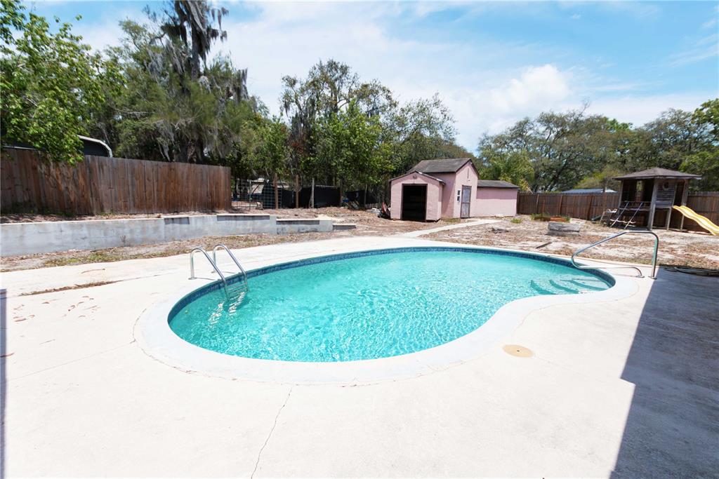 A backyard features an in-ground swimming pool, a pink shed, and a wooden play set — 9939 WOODRIDGE COURT, PORT RICHEY, FL