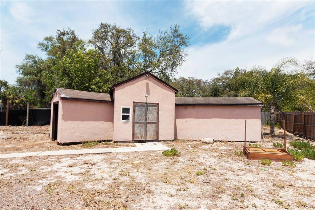 A pink, single-story shed with double doors sits on a sandy lot with trees — 9939 WOODRIDGE COURT, PORT RICHEY, FL