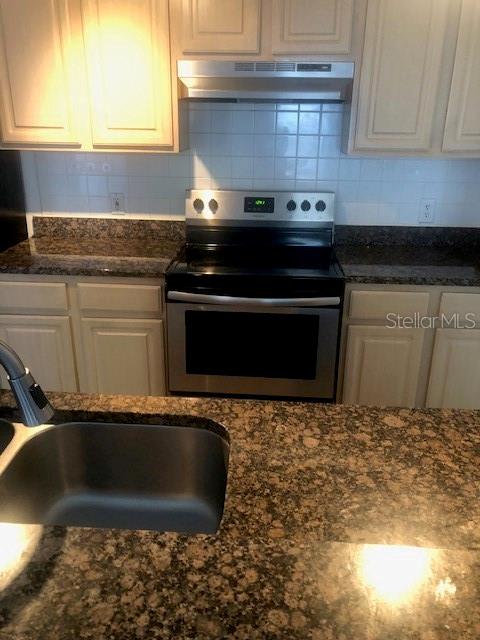 A kitchen features granite countertops, a stainless steel stove, and light-colored wooden cabinets — 413 SUMMIT RIDGE PLACE UNIT 305, LONGWOOD, FL