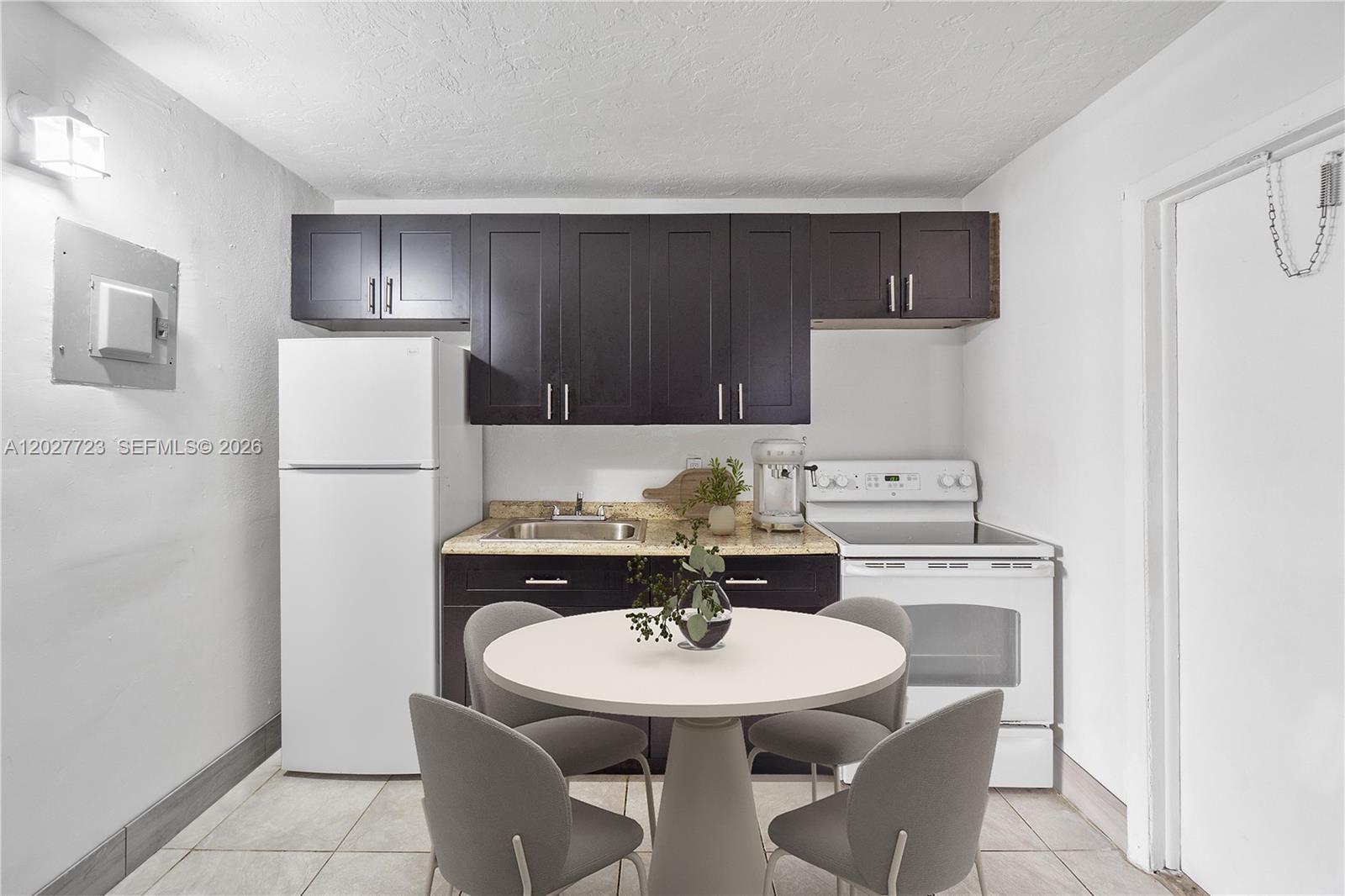 A small kitchen features dark cabinets, white appliances, a round dining table, and tile flooring — 332 SW 3rd St # 5, Belle Glade FL 33430, BELLE GLADE, FL