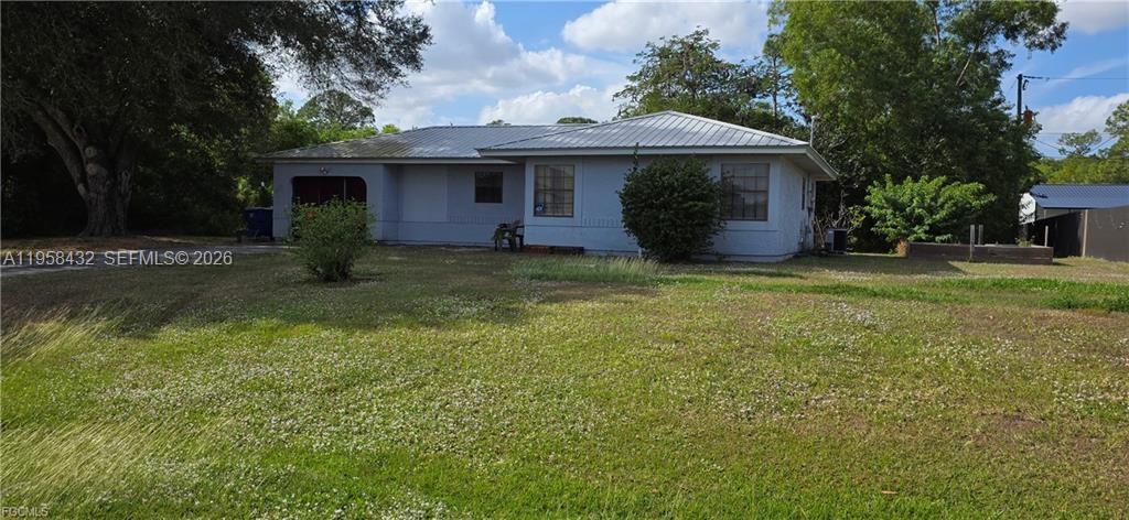 A single-story house with a light-colored exterior and a metal roof sits on a lawn — 5036 E Tradewinds Cir, La Belle FL 33935, LA BELLE, FL