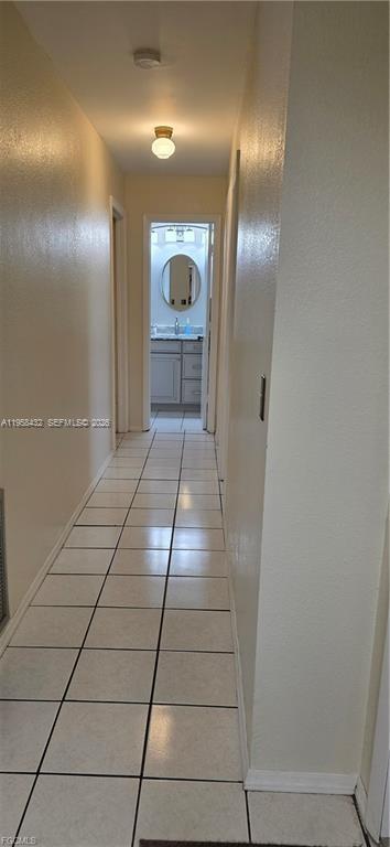 A hallway with white tile flooring leads to a bathroom with a vanity and mirror — 5036 E Tradewinds Cir, La Belle FL 33935, LA BELLE, FL