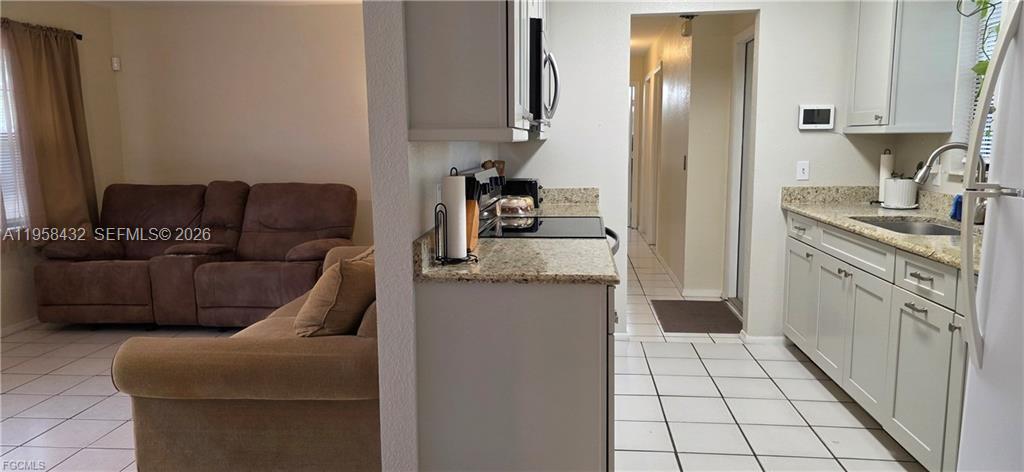 A kitchen with light-colored cabinets and granite countertops sits adjacent to a living room area — 5036 E Tradewinds Cir, La Belle FL 33935, LA BELLE, FL