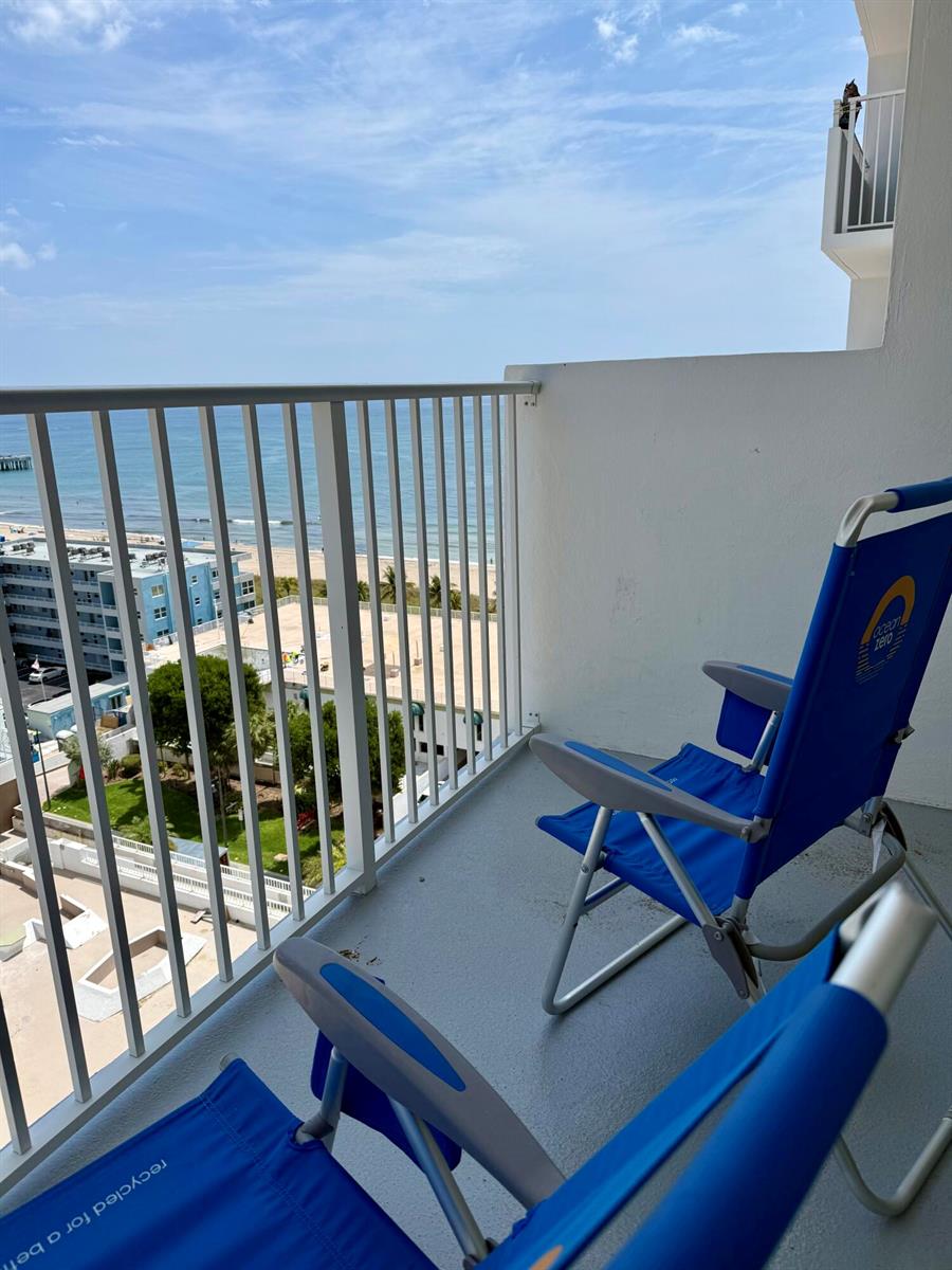 A balcony with two blue folding chairs overlooks the ocean and a nearby building — 111 Briny Avenue # 1405, Pompano Beach FL 33062, POMPANO BEACH, FL