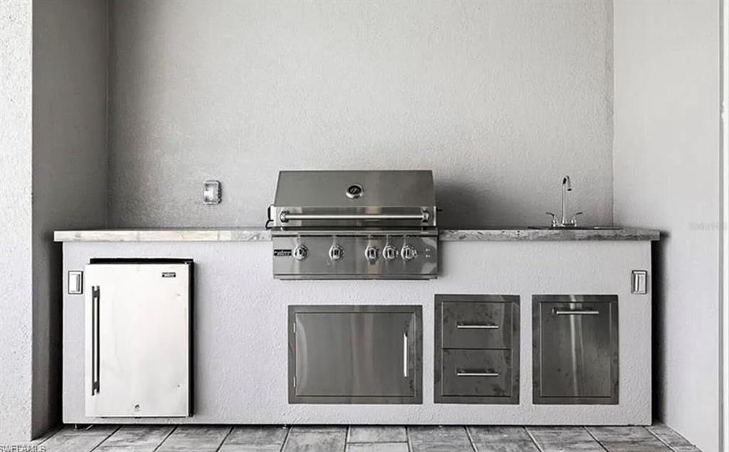 An outdoor kitchen features a stainless steel grill, sink, refrigerator, and storage cabinets — 2153 NW 18TH AVENUE, CAPE CORAL, FL